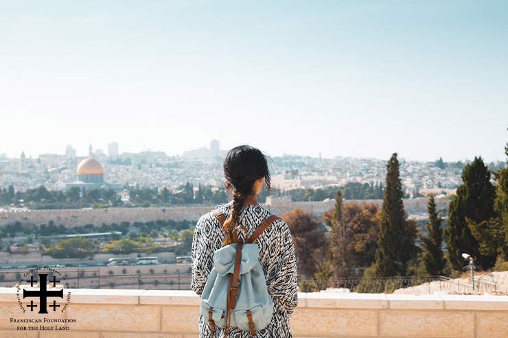 Young girl wearing backpack looks over Holy Land